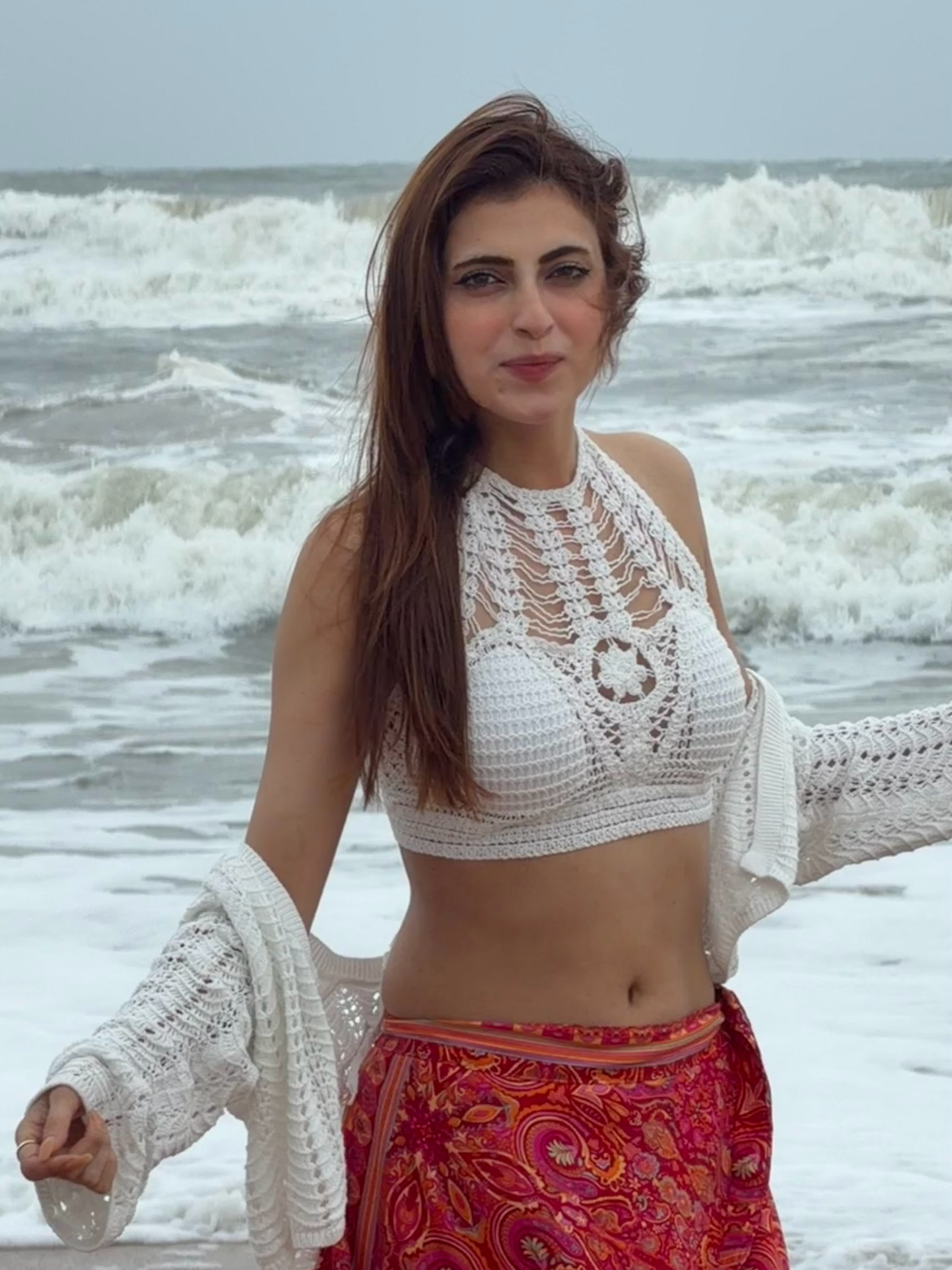 Farrhana Bhatt adds a bold touch with a vibrant red printed skirt that flows beautifully against the ocean backdrop.