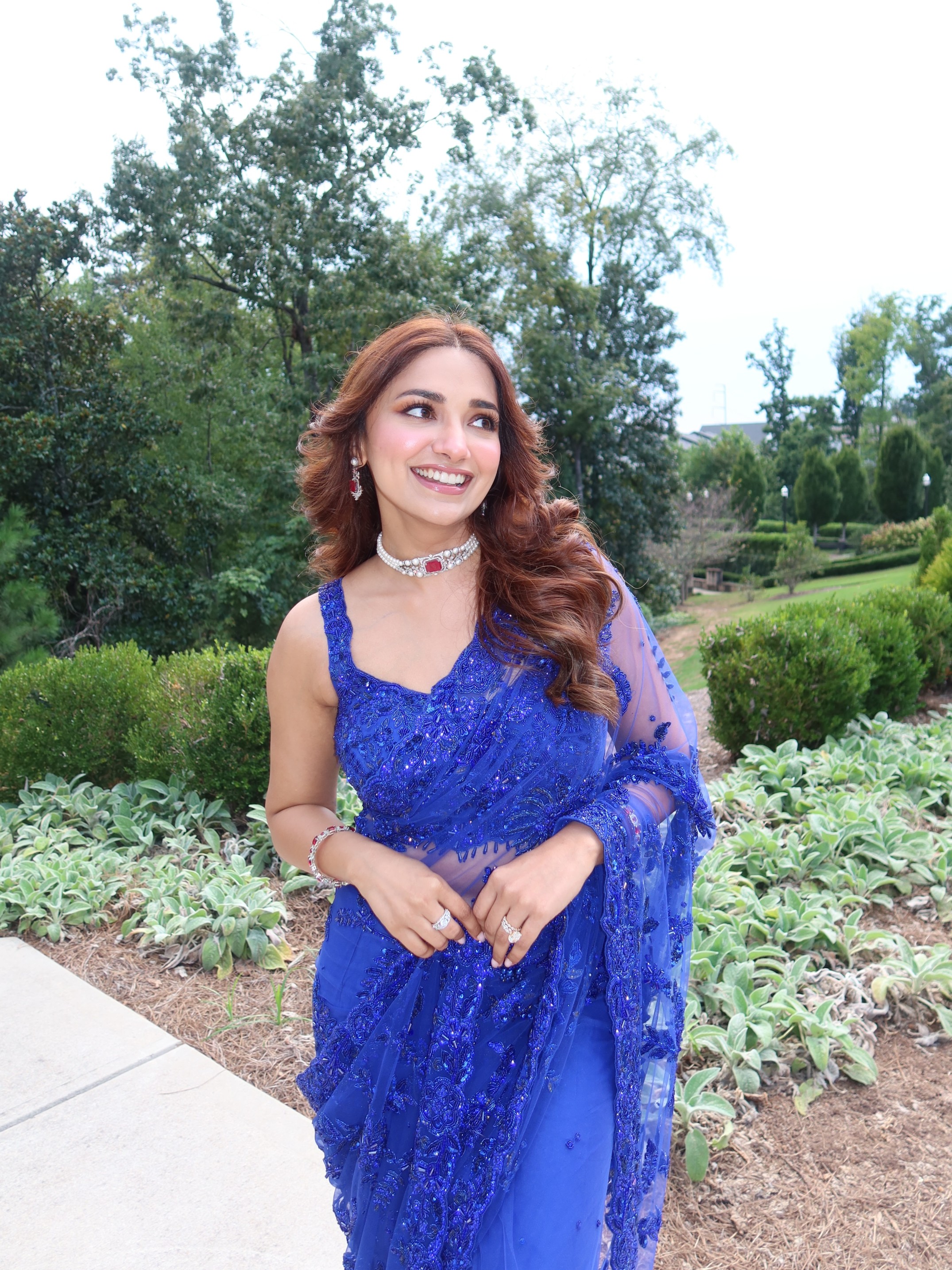 The striking blue ensemble features a matching sleeveless blouse and a beautifully embroidered drape that adds movement, texture, and undeniable red-carpet appeal.