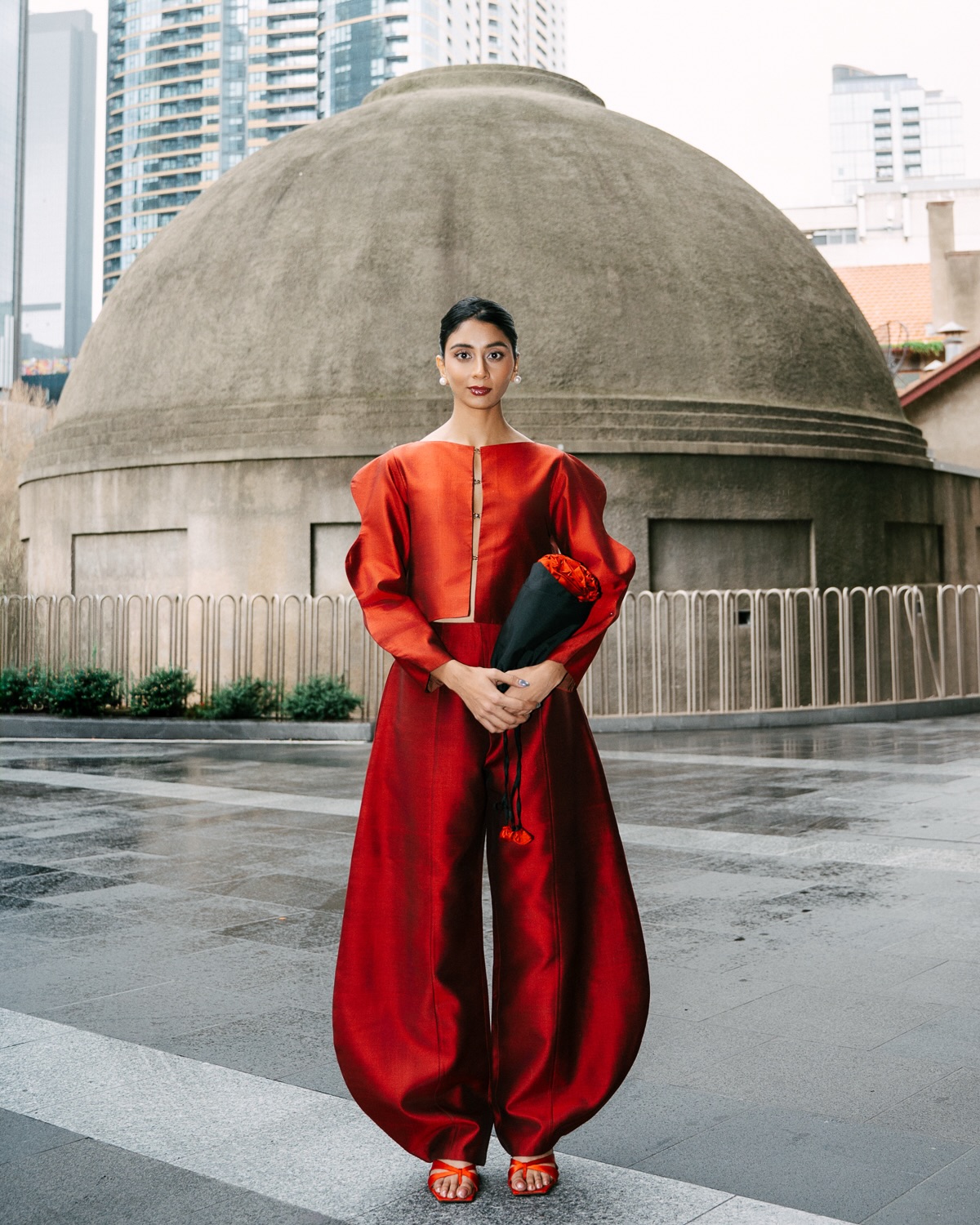 Dolly Singh complements the monochrome look with a sleek black clutch, delicate earrings, and matching red heels that add the perfect finishing touches.