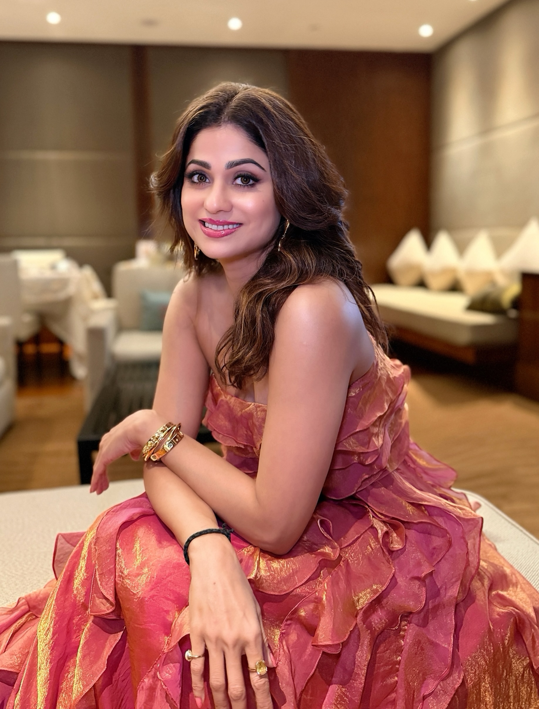 Shamita Shetty opts for bronzed makeup, softly defined eyes, and a nude lip, while her voluminous wavy hair perfectly complements the outfit's romantic vibe.