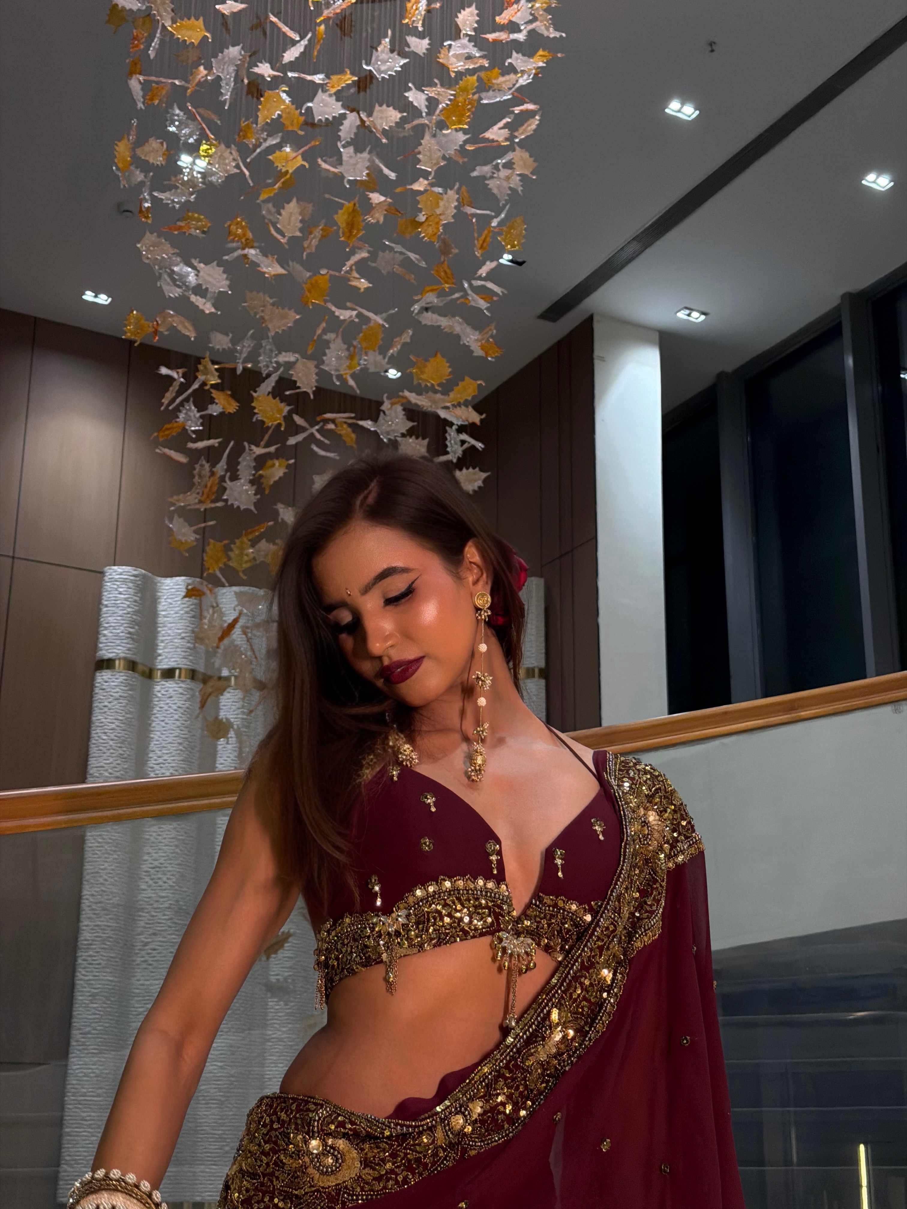 Nancy Tyagi stuns in a rich maroon saree featuring ornate gold embroidery along the borders. The elegant drape adds a timeless touch to her look.